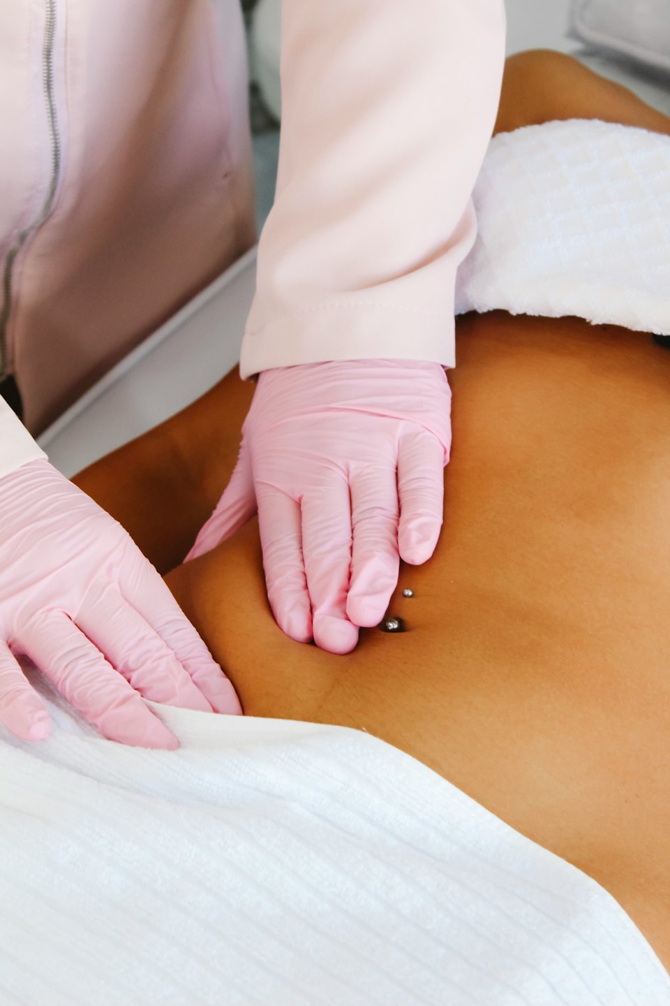 Mani guantate eseguono un trattamento spa su un addome con piercing all'ombelico.